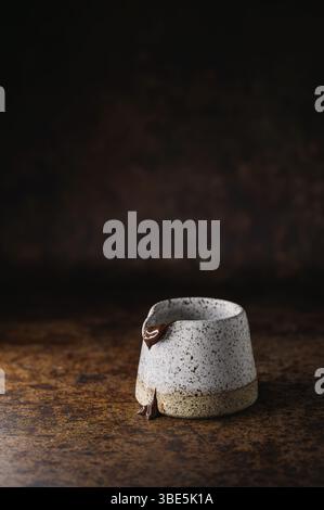 A white speckled ceramic cup with chocolate dripping beautifully down its sides. It is placed on a textured, rustic surface, creating a warm, cozy amb Stock Photo
