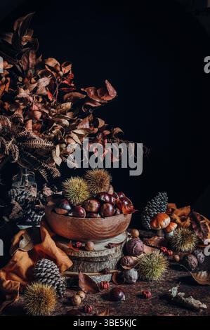 A beautifully arranged autumn scene featuring a bowl of chestnuts, surrounded by dried leaves, pine cones, and rustic wooden elements, creating a warm Stock Photo