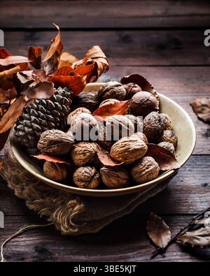 A cozy autumn still life featuring a bowl of walnuts, pine cone, and dried leaves on a rustic wooden table, capturing the essence of the fall season w Stock Photo