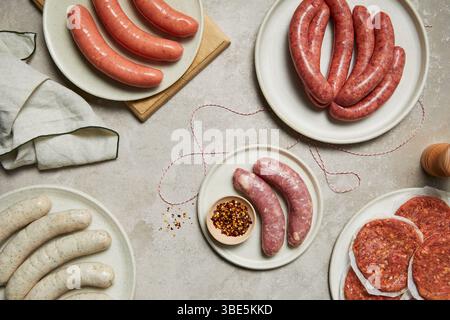 An assortment of sausages and meats displayed on white plates, showcasing a variety of textures and colors, alongside spices, embodying a butcher shop Stock Photo
