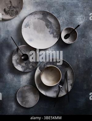 Top view of a sophisticated arrangement of ceramic tableware featuring plates and bowls with a unique design, perfectly placed on a textured dark grey Stock Photo