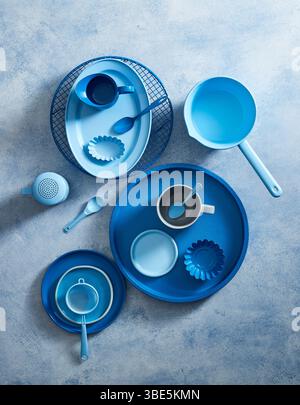 Top view of a stylish blue ceramic crockery set arranged on a textured gray background. The set includes plates, bowls, cups, and utensils, all showca Stock Photo