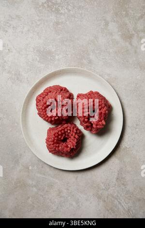 Three mounds of freshly ground beef presented on a white ceramic plate. The meat's rich red color and texture provide a vivid display, perfect for cul Stock Photo