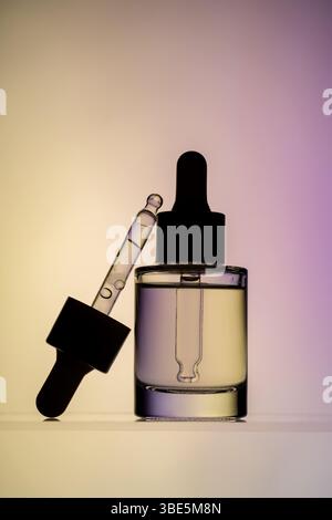 A stylish image showing a clear face serum bottle with a dropper, set against a soft pink and yellow gradient background. Ideal for beauty and skincar Stock Photo