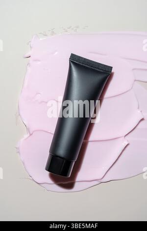 A sleek black cosmetic package lies atop a textured spread of pastel pink cream, creating a striking visual contrast. Ideal for beauty product present Stock Photo