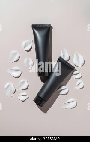 Two sleek black cosmetic tubes placed on a neutral background accompanied by white cream smears, highlighting modern skincare packaging and product el Stock Photo