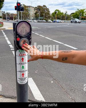 A close-up of a hand with red nail polish pressing a crosswalk button at a busy intersection in Melbourne, Australia, illustrating urban life and pede Stock Photo