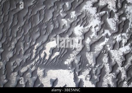 From above intricate patterns of black sand adorned with subtle white shades, creating a visually stunning textural landscape. Stock Photo