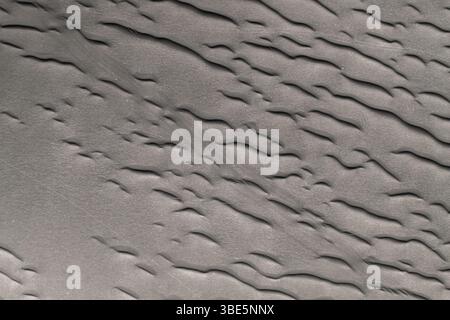 A detailed image capturing the unique textures and wavy patterns of natural black sand. This photo highlights the fine details and contrast found in b Stock Photo