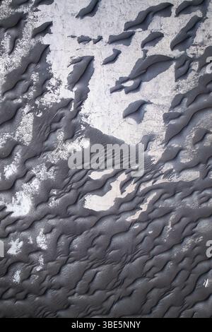 Close-up image capturing the intricate textures of black sand alongside peeling white paint, emphasizing natural and man-made contrasts. Stock Photo