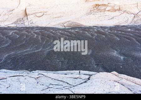 A detailed image capturing the contrast between the rippled black sand and cracked white rock, emphasizing the unique textures of each. Stock Photo