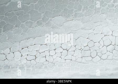 Overhead view of saline mud cracked into abstract patterns resembling natural formations. The white and grey tones create a visually striking landscap Stock Photo