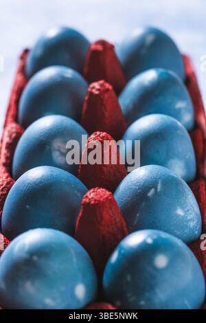 Vibrant blue Easter eggs neatly arranged in a bold red egg carton, shot from above. The contrasting colors create a striking visual. Stock Photo