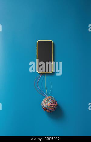 A conceptual image showing a smartphone connected to a ball of colorful string, symbolizing the complex impact of the Internet Stock Photo