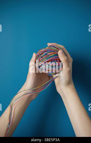 Hands holding a colorful ball of wires symbolizing the complex impact of the internet on children's development, learning, and connectivity in a digit Stock Photo