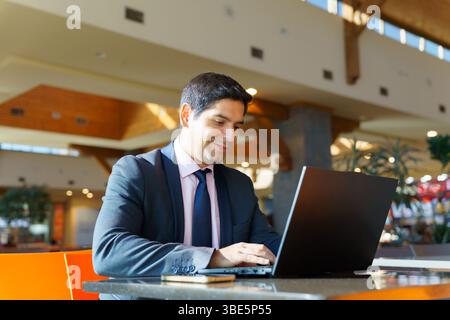 Young Chilean businessman in a sleek suit working diligently on his laptop in a bright, modern space. The environment reflects professionalism and foc Stock Photo