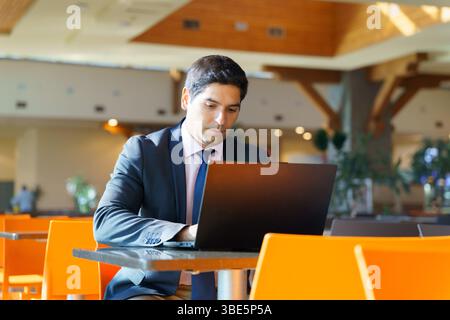 A focused young Chilean businessman working on his laptop in a modern cafe. He is dressed in a professional suit, highlighting his commitment and dedi Stock Photo