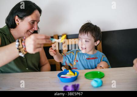 A child with Down syndrome and his mother sitting at a table engage in a creative and joyful play session with colorful clay. The playful interaction Stock Photo