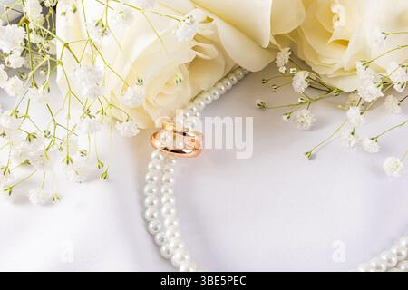 Elegant wedding rings are showcased with delicate white flowers and pearls against a soft white fabric backdrop, creating a sophisticated and romantic Stock Photo