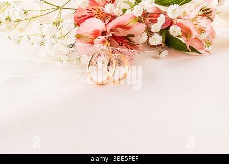 Elegant composition of two gold wedding rings surrounded by delicate pink and white flowers on a soft white surface, symbolizing love and commitment i Stock Photo