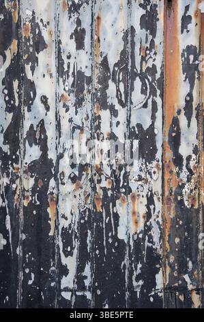 Abstract background. Weathered, dilapidated garage door with textures and colours of flaking paint and rusting metal. Contrasting light and dark tones. Stock Photo