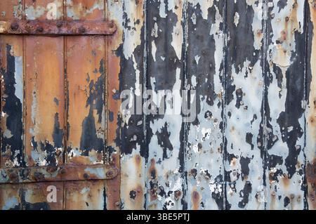 Abstract background. Weathered, dilapidated garage door with textures and colours of flaking paint and rusting metal. Contrasting light and dark tones. Stock Photo