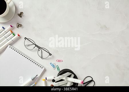 From above a neatly organized creative workspace featuring a sketchbook, colorful markers, glasses, and office supplies on a marble table, with a back Stock Photo