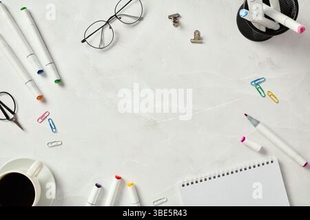 Top view of an organized creative workspace setup featuring a sketchbook, assorted marker pens, a cup of coffee, and glasses on a marble table backgro Stock Photo
