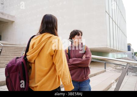 Two teenagers, one non-binary and the other female, engage in a thoughtful conversation on their school campus, highlighting themes of friendship and Stock Photo