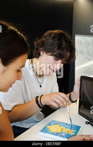 Two smiling teenagers, a non-binary individual and a female, joyfully engage in a creative painting session as part of their school activities, highli Stock Photo