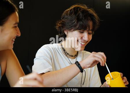 Two happy teenagers, a non-binary individual and a female, are engaged in a joyful artistic activity. They both express creativity and friendship whil Stock Photo
