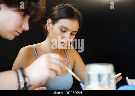 Two engaged teenagers, a non-binary individual with short hair and a female, collaborate on a painting project in an art class, emphasizing creativity Stock Photo