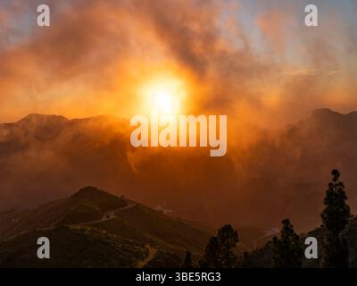 Dramatic sunset lighting up the clouds and mist over the mountains, viewed from Cruz de Tejeda in Gran Canaria, with Roque Nublo in the distance. Stock Photo