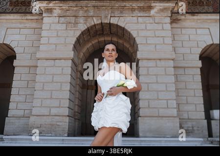 A stunning bride in a white dress poses elegantly in front of an ancient villa in Treia, Macerata, Italy, capturing the beauty and romance of an Itali Stock Photo