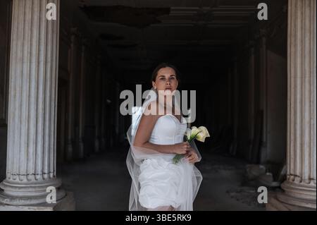 A bride in a stunning white gown poses gracefully in an ancient villa in Treia, Macerata. The setting, with its grand columns, adds charm to this time Stock Photo