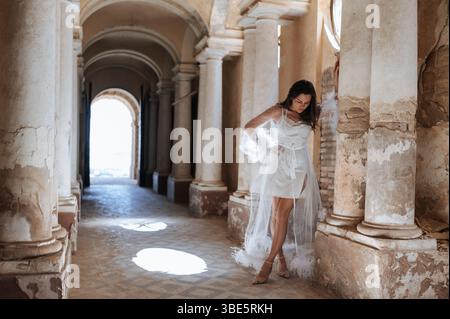 A bride poses elegantly in a flowing white gown amidst the historic architecture of an ancient villa, capturing the romance and charm of a wedding in Stock Photo