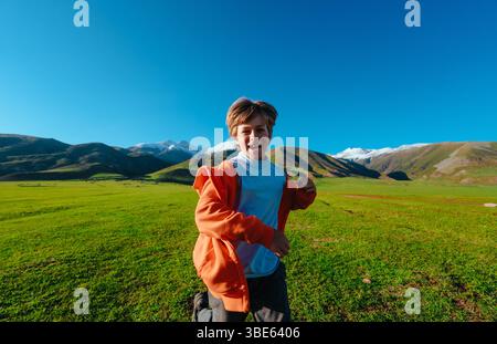 Boy running through a green meadow in the mountains on a sunny summer day Stock Photo
