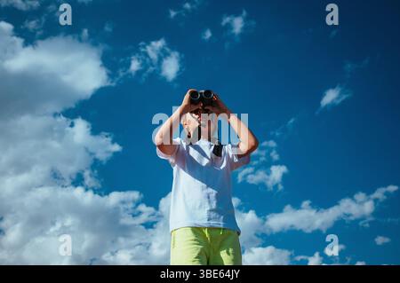 Portrait of boy looking in binoculars on blue sky background Stock Photo
