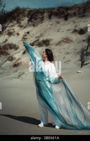 woman in white clothes dancing with blue cloth on the beach Stock Photo