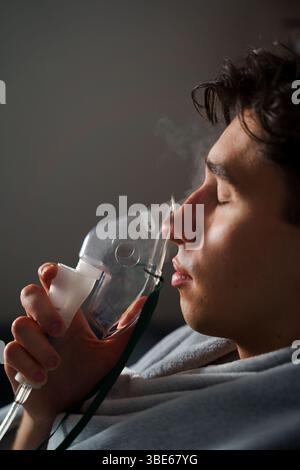Using compressor nebulizer for disease treatment at home. Man inhaling through oxygen mask for cough treatment Stock Photo