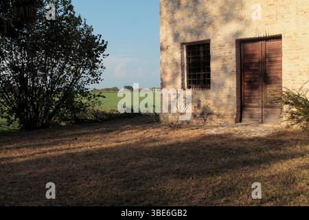 Yellow brick ruins of and old church in the countryside, under the warm light of the late afternoon sun, the shadow of trees stretches on the wall. Stock Photo