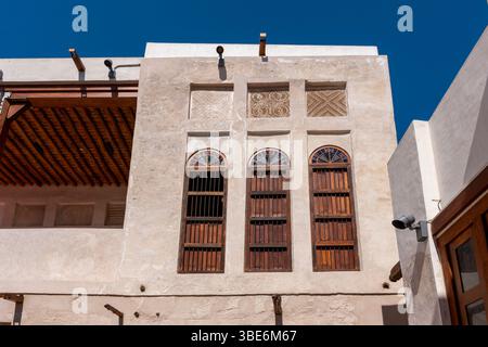 Three arched windows with wooden shutters frame the white facade at Al-Jalahma House on the Pearling Path in Muharraq under bright blue sky. Stock Photo