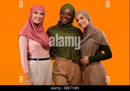 Three Muslim Ladies In Hijab Headscarf Standing Over Yellow Background Stock Photo