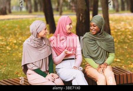 Muslim Young Women Talking Sitting On Bench In Park Outdoors Stock Photo