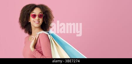 Happy young african american lady in trendy red glasses holds colored packages Stock Photo