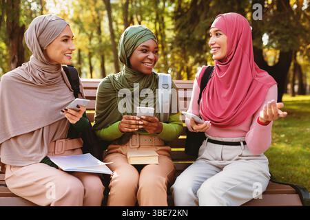 Muslim Women Using Phones Talking And Having Fun In Park Stock Photo