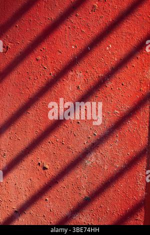 Concrete painted red with a shadow from a fence. Rustic background Stock Photo