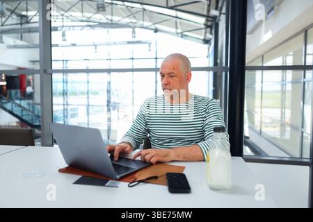 Businessman in striped shirt using computer at airport, digital nomad lifestyle. Stock Photo