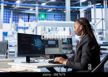 Engineer coding in solar panel plant, using artificial intelligence to automate equipment processes. Photovoltaics factory programmer writing scripts to optimize robotic operations using AI tech Stock Photo