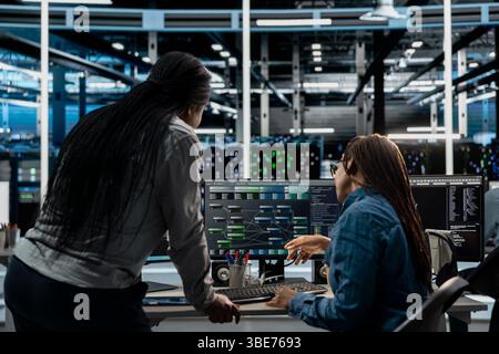 Server room manager overseeing work done by engineer using artificial intelligence to reduce downtime. Team leader supervising employee implementing AI driven solutions for data center equipment Stock Photo